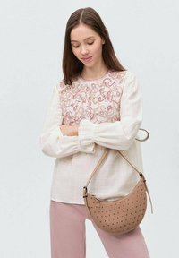 Béžová blúzka s ružovou výšivkou na yoke, s balónovými rukávmi a okrúhlym výstrihom. Béžová crossbody taška s perforáciami.