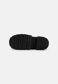 Black rubber shoe sole with pronounced ridges and textured surface for grip, featuring a rounded toe and flat heel design.