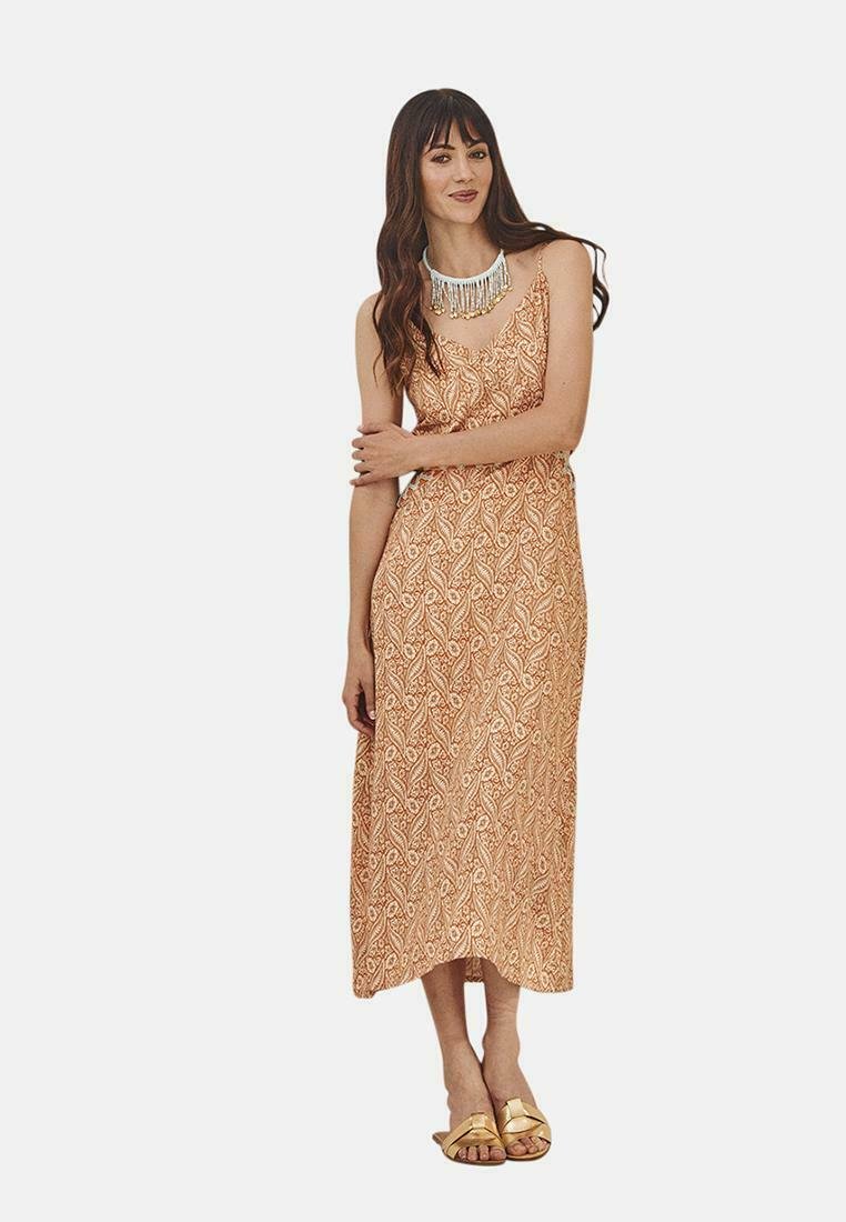 Vestido maxi de tela melocotón con un patrón de paisley; diseño sin mangas, ligera forma en A, complementado con un collar de cuentas y sandalias doradas.