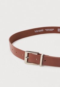 Belte af coated læder i brun med en glat overflade. Har en sølvmetalspænde og en række huller til justering.