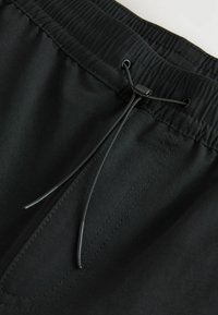 Shorts negri cu talie elastică și închidere cu șnur, având o textură netedă și detalii de cusături contrastante.