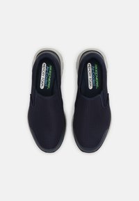 Marinblå slip-on-skor med ventilerande mesh-övre, lätt grå sula och "Skechers Air Cooled Memory Foam"-m ärkning på innersulan.