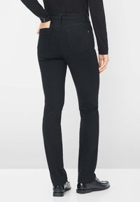 Jeans neri slim-fit con una trama liscia, design a cinque tasche e dettagli di cucitura sottili. Indossati con mocassini neri lucidi.