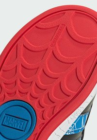 Svart sneaker sula med röd gummibotten som har ett texturerat spindelnätmönster, blå cirkulär detalj med "MARVEL"-logotyp och icke-märkande design.