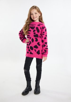 Fluffy roze sweater met zwarte luipaardvlekken, lange mouwen en brede halslijn, gecombineerd met zwarte skinny jeans en zwarte enkellaarsjes.