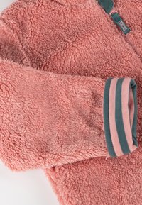 Giacca in pile di un morbido rosa con una finitura texturizzata. Presenta un polsino rigato in teal e rosa e un dettaglio con zip con etichetta del brand.