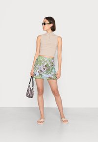 Top crop justo bege canelado com fecho, saia mini em padrão floral vibrante, mala listrada em preto e branco e sandálias claras.