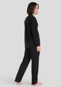 Conjunto de loungewear negro que incluye una camiseta de manga larga con cuello redondo y pantalones a juego. Tejido suave con un corte holgado y un diseño minimalista.