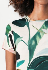 Lyhythihainen paita, jossa on kerma väri ja vihreä lehtikuvio, puuvillamateriaali, käytännöllinen pyöreä kaula-aukko sekä kevyt, sileä rakenne.