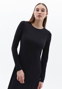 Schwarzes langärmliges Kleid in taillierter Form, aus glattem Stoff mit runder Halslinie und dezenten Seitennähten.