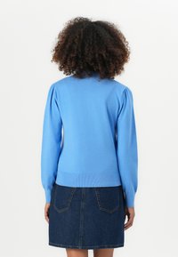 Lys blå striktrøje med puffede ærmer, ribbede manchetter og kant, parret med en denimnederdel. Glat tekstur, afslappet design.