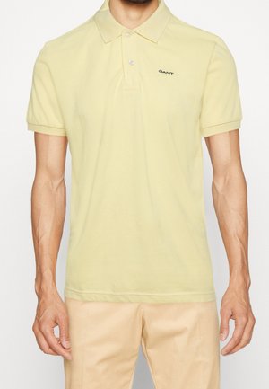 Polo en coton jaune à manches courtes, logo noir sur la poitrine et col classique. Le tissu a une texture douce.