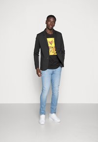 Sort blazer over en grafisk sort og gul t-shirt, lyseblå jeans og hvide sneakers. Glatte teksturer med en skræddersyet pasform.