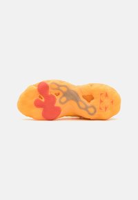 Semelle de chaussure en caoutchouc orange avec un motif en chevrons texturé. Présente un accent rouge en caoutchouc bien visible et des découpes pour plus de flexibilité.