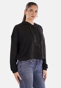 Felpa nera corta con zip frontale, cappuccio regolabile con cordino e polsini a coste, abbinata a jeans in denim blu con una vestibilità comoda.