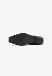 Suela de zapato de goma negra con una superficie texturizada, que presenta una forma cónica y ranuras horizontales para tracción. Bordes lisos y diseño minimalista.