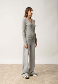 Grau zipfelpullover mit langen Ärmeln, kombiniert mit hellgrauen, weiten Jeans und Sneakers mit geometrischem Muster. Flacher Hintergrund.