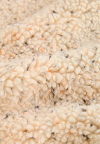 Tissu en polaire de couleur crème douce avec de petites taches noires et orange, présentant une surface texturée, duveteuse et épaisse.