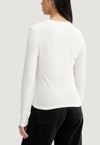 Biała koszula z długim rękawem i okrągłym dekoltem, dopasowana, wykonana z miękkiej bawełny o gładkiej fakturze. Połączona z czarnymi dżinsami.