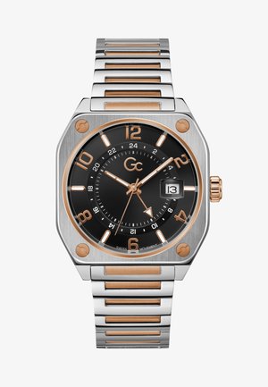 Négyzet alakú rozsdamentes acél óra fekete számlappal, rózsaarany díszítésekkel és óragyűrűkkel. Dátumablakkal és fém láncszíjjal rendelkezik.