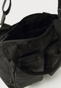 Bolso mensajero negro con un interior espacioso, bolsillos con cremallera, correas ajustables y una textura de tela suave y duradera.