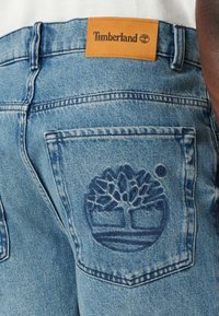 Blaue Denim-Jeans mit einem Leder-Logo-Patch von Timberland und einem gestickten Baumemblem auf der Gesäßtasche. Klassisches Design und Textur.