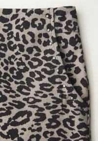 Harmaa kangas, jossa on musta leopardikuosi, koristeelliset hopeiset niitit sivuilla ja sileä, teksturoidun näköinen pinta.