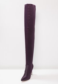 Botas ajustadas hasta el muslo en satén púrpura profundo. Punta afilada con un alto tacón stiletto. Textura suave con una silueta elegante.