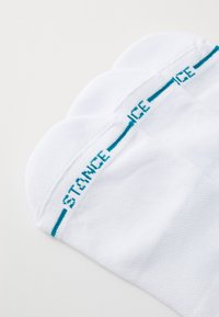White crew socks made of cotton blend, featuring a turquoise knitted band with the word "STANCE" across the top. Smooth texture, seamless design.