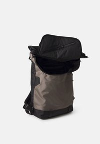 Sac à dos en tissu gris foncé avec des accents noirs. Il dispose d'un compartiment supérieur zippé, de bretelles rembourrées et d'un grand compartiment principal ouvert pour le rangement.
