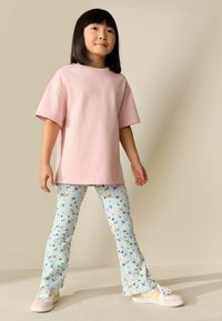 Maglietta rosa in cotone con maniche corte, abbinata a leggings svasati azzurri con motivi floreali. Completa l'insieme un paio di sneaker bianche e rosa.