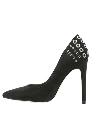 Sort ruskind stiletto højhælet sko med spids tå og metallic øjendetaljer omkring hælområdet.