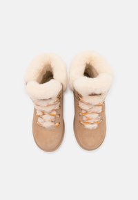 Beige Wildleder-Stiefeletten mit einer flauschigen cremefarbenen Schaffellbündchen, ausgestattet mit orangefarbenen und grauen Schnürsenkeln und einem runden Zehendesign.