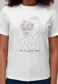 Hvit bomull t-skjorte med et svart linjetegning av et ansikt dekorert med rosa blomster. Teksten under lyder "Ta vare på sinnet ditt."