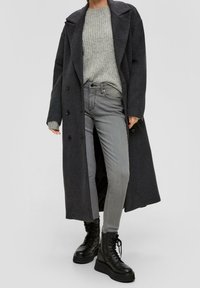 Long manteau en laine gris avec de grands revers et des boutons, associé à un pull en maille gris clair et un jean skinny gris. Bottines noires à lacets.