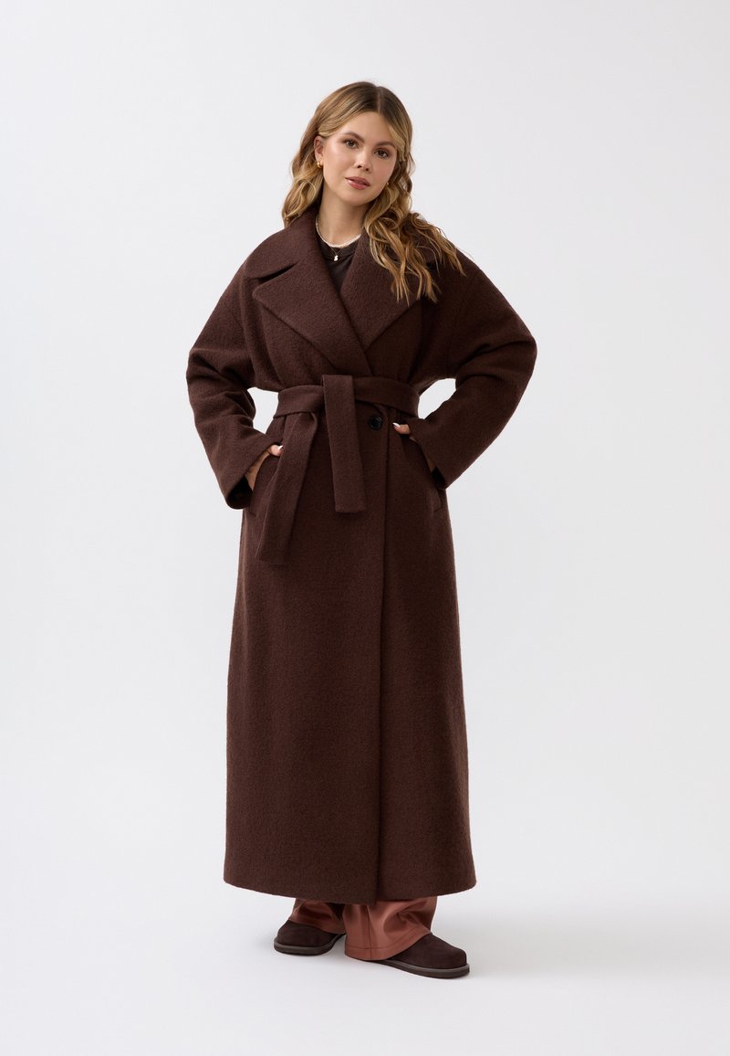 Brauner Wollmischmantel mit tailliertem Gürtel, breiten Revers und langen Ärmeln. Der Mantel hat eine lockere Passform und reicht bis zur Mitte der Waden.