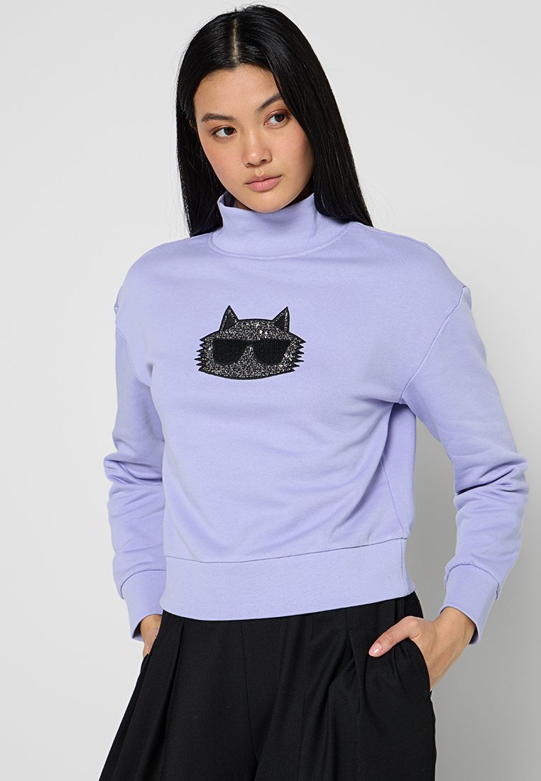 Sudadera lila con cuello alto; presenta un diseño de cara de gato negra con purpurina y gafas de sol; material suave y corte corto.
