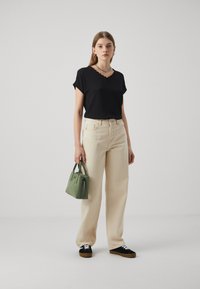 Svart topp med korte ermer og scallop-hals, beige vide bukser, grønn håndveske og svarte sneakers med hvite snørebånd.