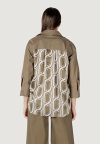 Camicia a maniche lunghe con il davanti color khaki e il retro con motivo che presenta disegni geometrici bianchi e beige. Realizzata in un tessuto liscio con colletto.