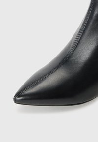 Scarpa nera in pelle con punta affusolata e texture liscia, caratterizzata da un sottile dettaglio di cucitura lungo il lato e una silhouette affusolata.