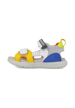 Sandal colorido que presenta materiales en amarillo, azul, blanco y gris. Diseño abierto con correas ajustables, suela texturizada y malla transpirable.