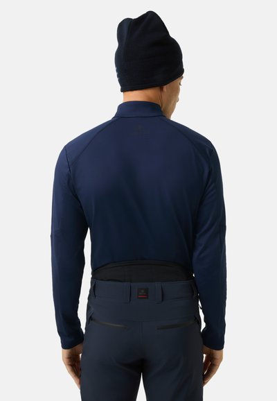 Navyblaues Langarmoberteil mit Stehkragen, glatter Textur und Logodetail. Kombiniert mit dunklen Hosen mit kontrastierenden Taschenakzenten.