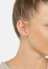 Silver star-shaped earrings with clear gemstones, featuring a sleek design that complements the ear and enhances sparkle.