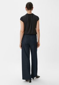 Top noir sans manches avec un dos froncé ; associé à un pantalon en denim taille haute et à jambe large de couleur bleu foncé ; conçu avec des poches arrière.