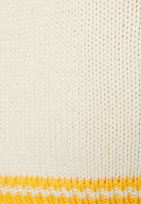 Sweater tricotado em creme com um padrão texturizado; apresenta um destaque amarelo forte na parte inferior e um elemento de design em zigue-zague.