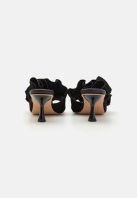 Sorte semskede høyhælte sko med rynkede detaljer bak, med en blank svart stiletthæl og en lys brune innersåle.