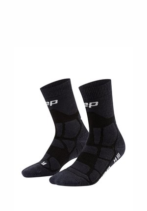 Paar schwarze Sportsocken mit weißem Logo und gepolsterten Bereichen für den Fußbogen, vor weißem Hintergrund dargestellt.
