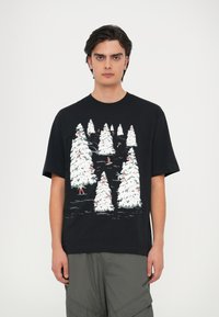 Must musta T-särk, millel on värvikas talvine stseen, kus on valged lumega kaetud puud ja väiksed tegelased suusatamas, trükitud pehme puuvillase kanga peale.