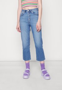 Calças de ganga azul claro, em corte cropped e perna reta, com fecho de cinco botões e bainha desfiada, combinadas com sapatos de plataforma roxos e meias.