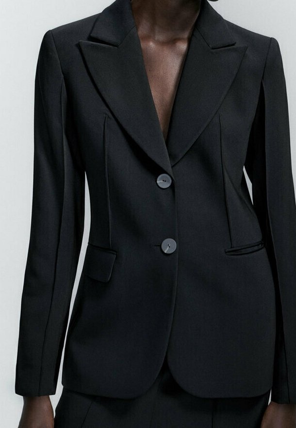Blazer noir cintré avec un col à revers cranté, une fermeture à deux boutons et des poches latérales. Tissu lisse avec des coutures structurées qui mettent en valeur une silhouette ajustée.